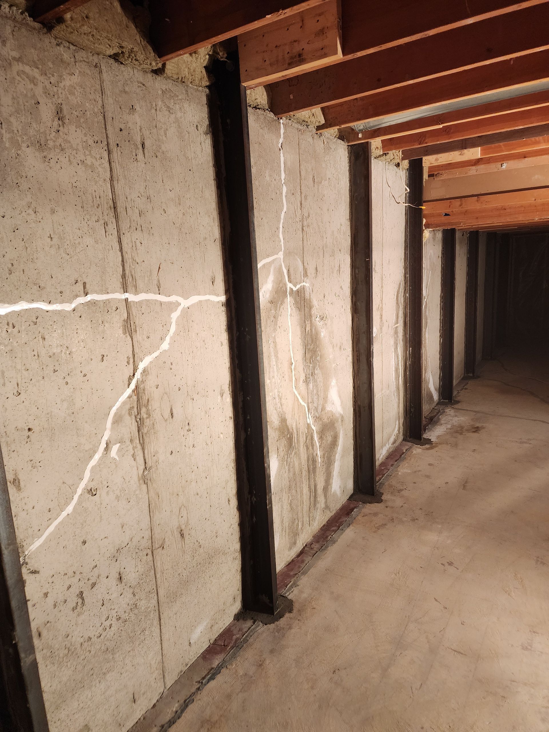 Concrete basement wall with vertical supports and cracks.