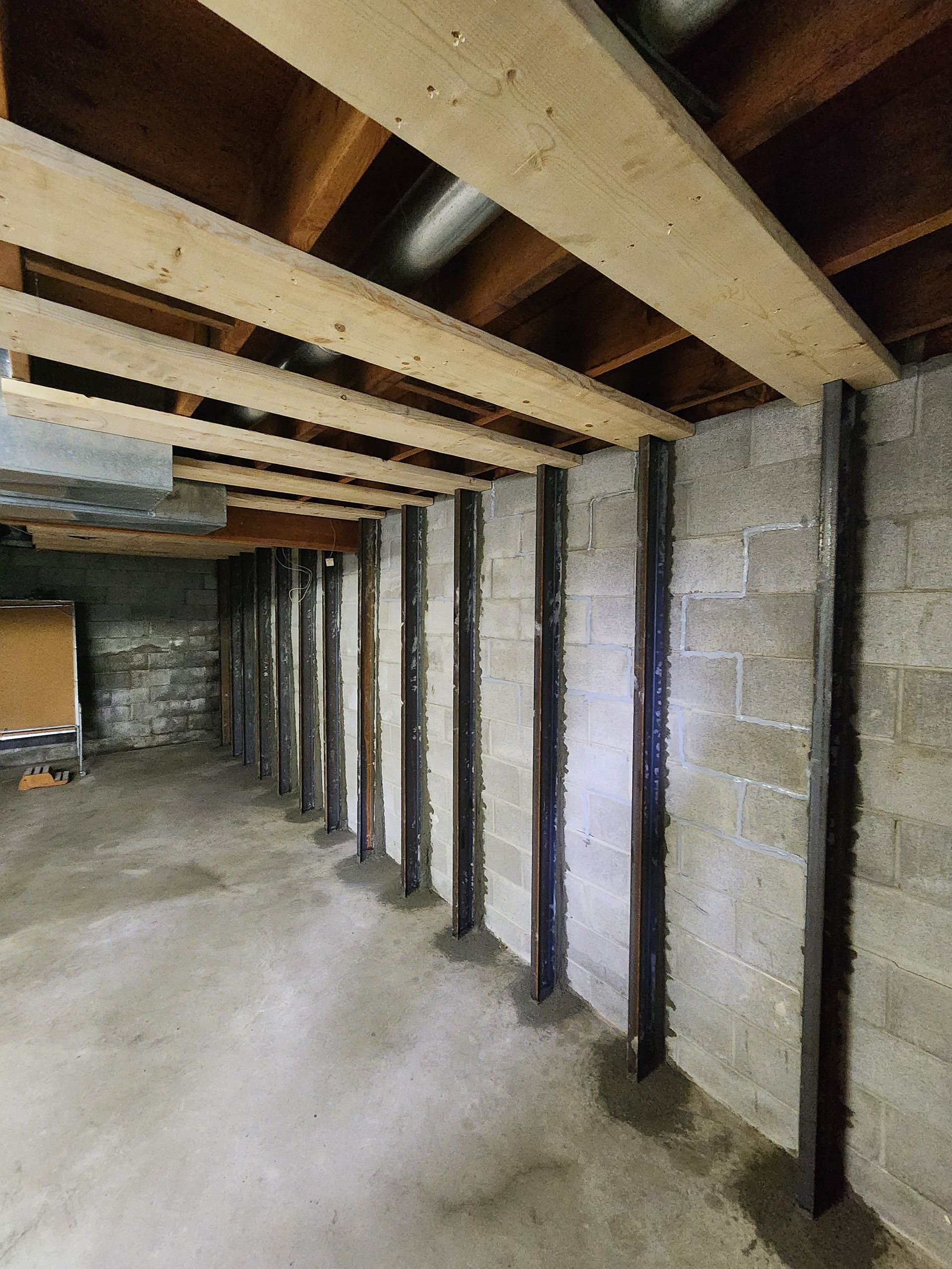 Basement with concrete block wall, supported by metal beams and wood planks; interior view.