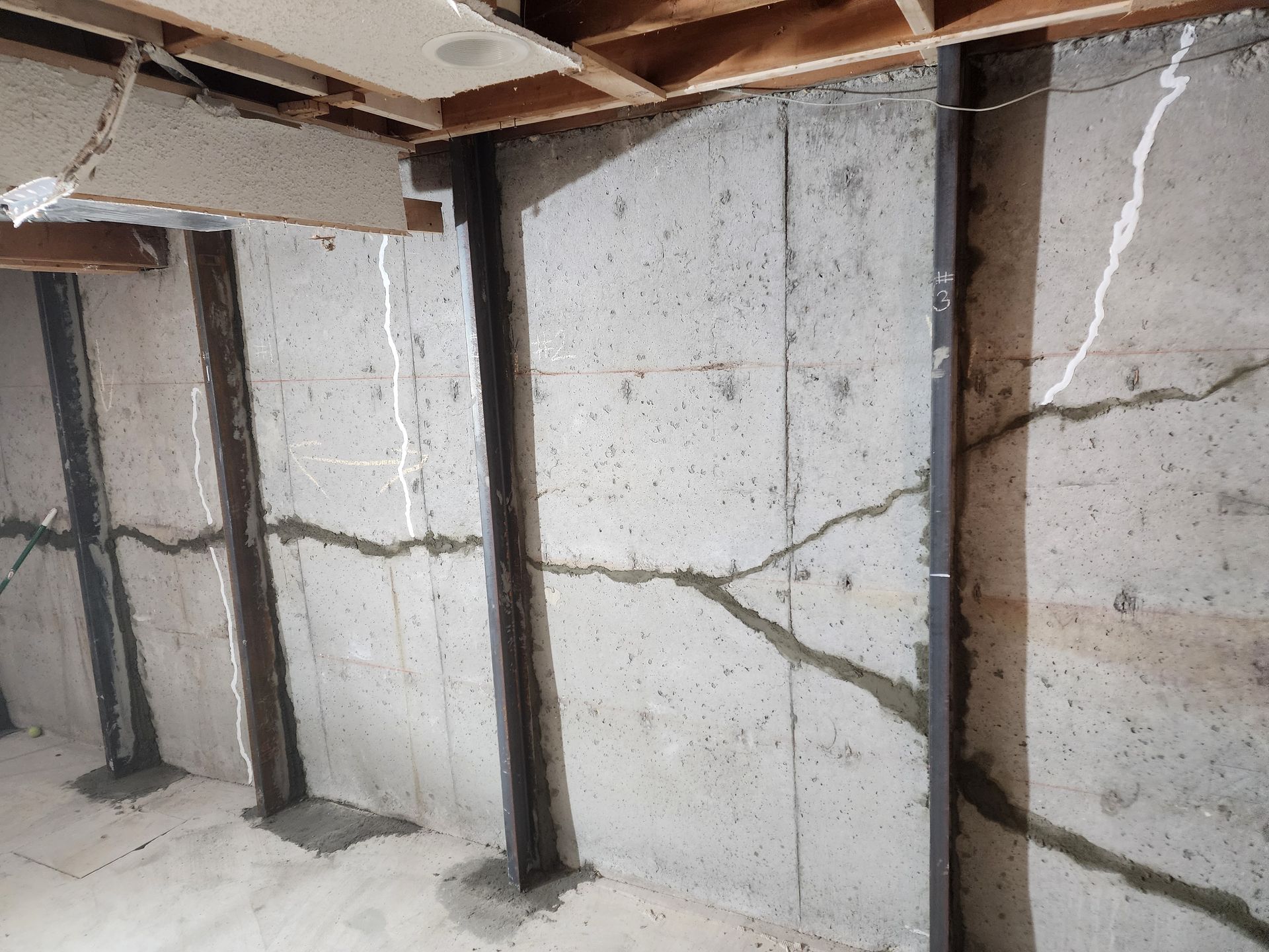 Basement wall with cracks, reinforced by steel beams, indicating structural damage.