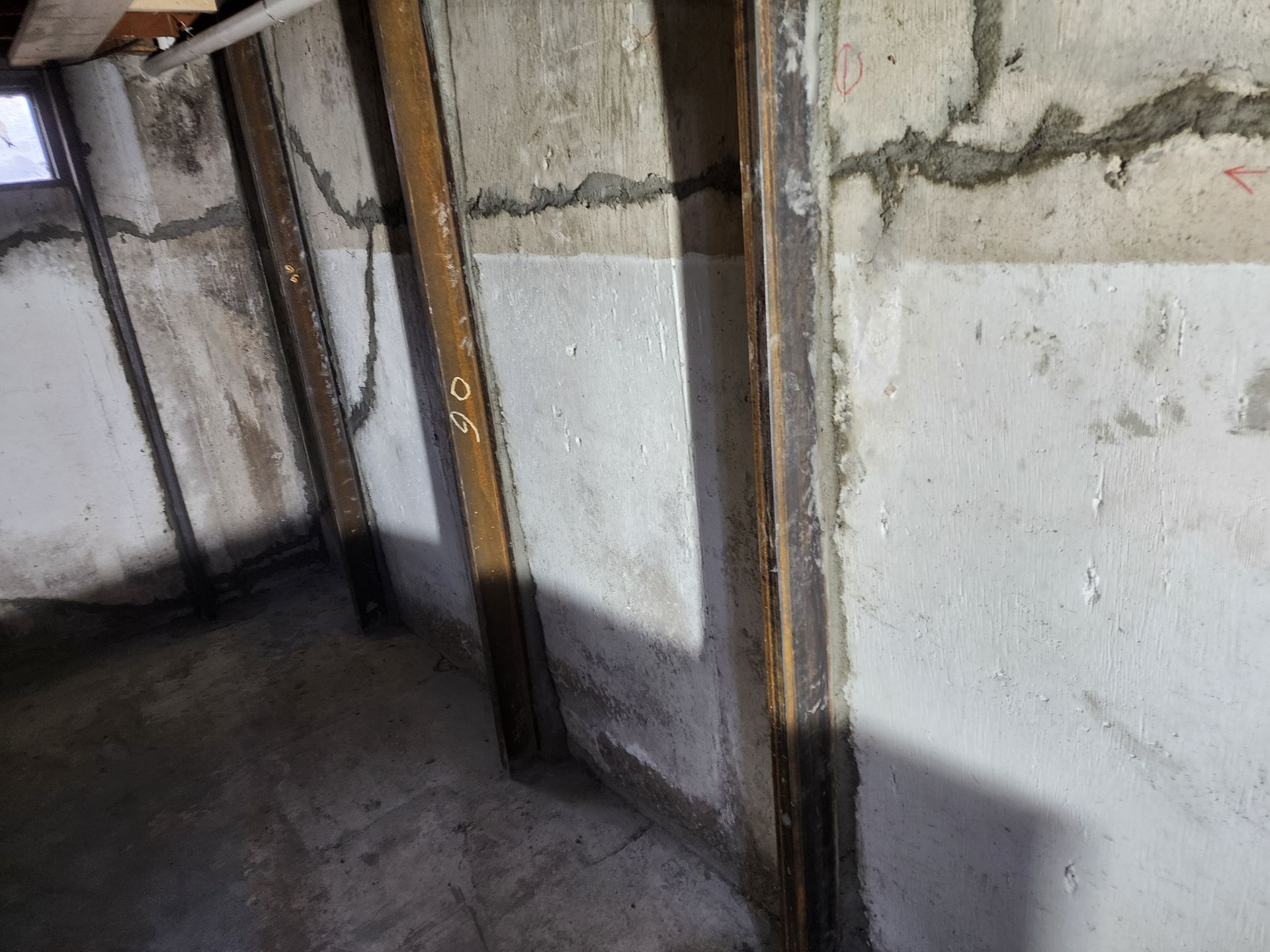 Basement interior with support beams against a concrete wall. Cracks sealed with gray sealant