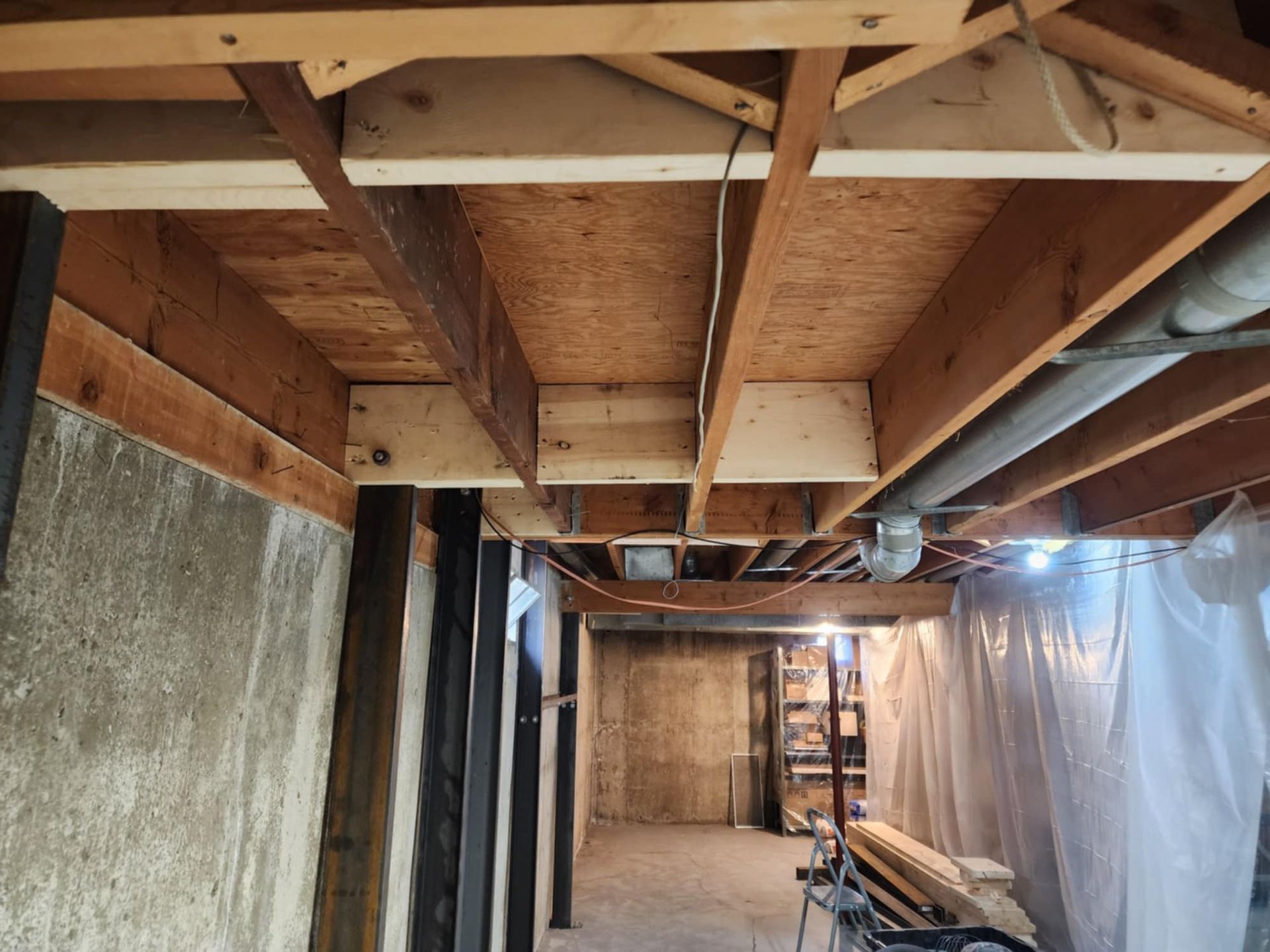 Basement ceiling with exposed wooden beams, concrete walls, and ductwork. Construction in progress.