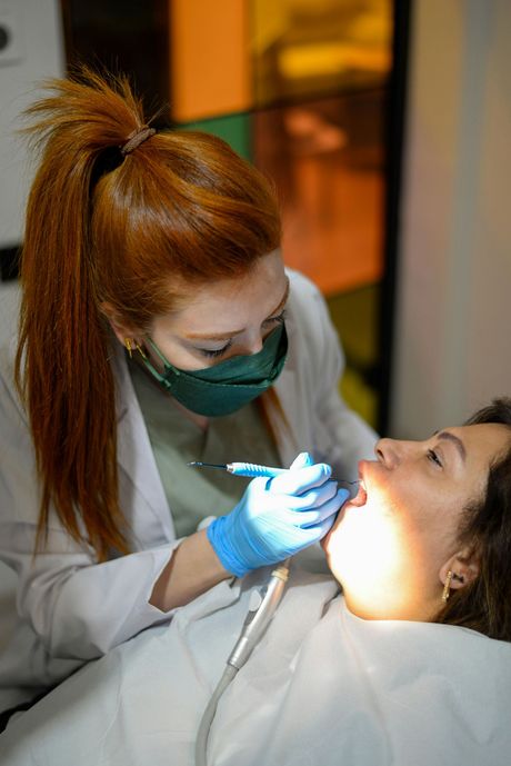 Dentist examining a patient’s open mouth with a dental tool and bright exam light