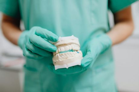 Dentist in teal scrubs holding a dental model with gloved hands