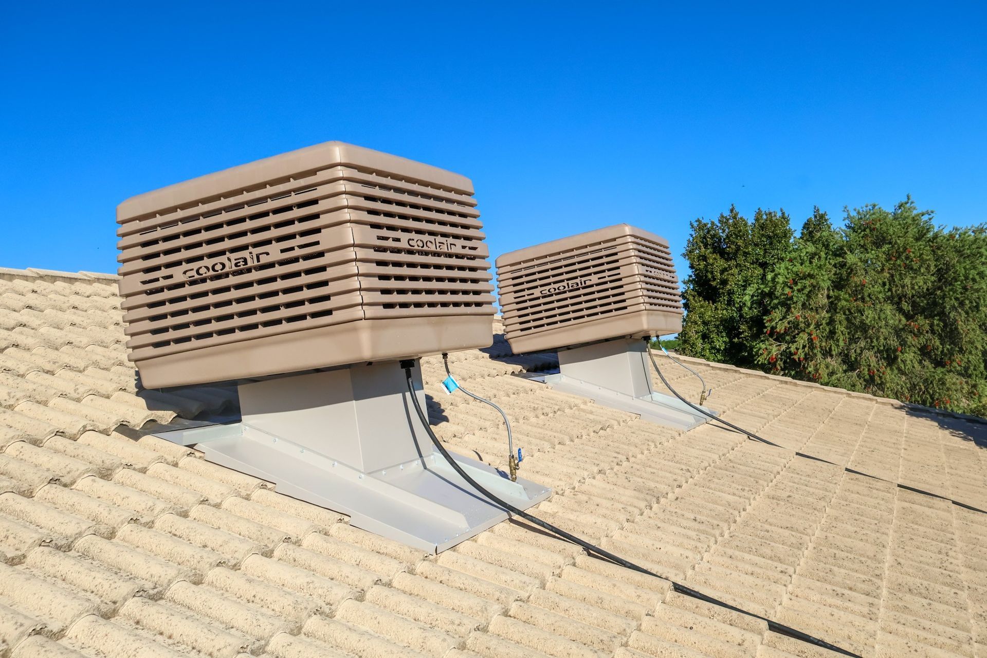 Two brown evaporative coolers on a beige-tiled roof against a clear blue sky.