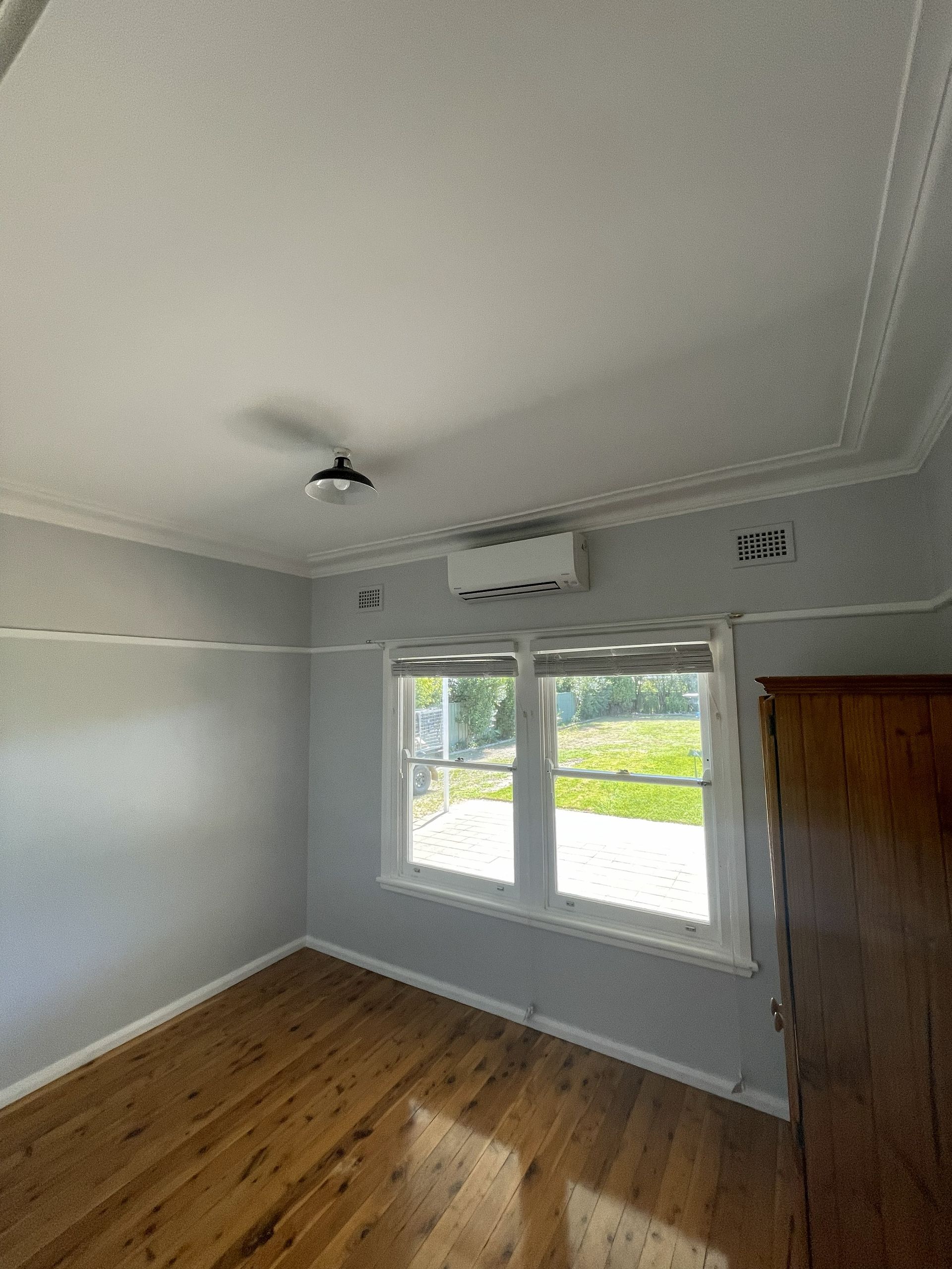 Empty room with wooden floor, two windows, air conditioner, and a dark ceiling light.
