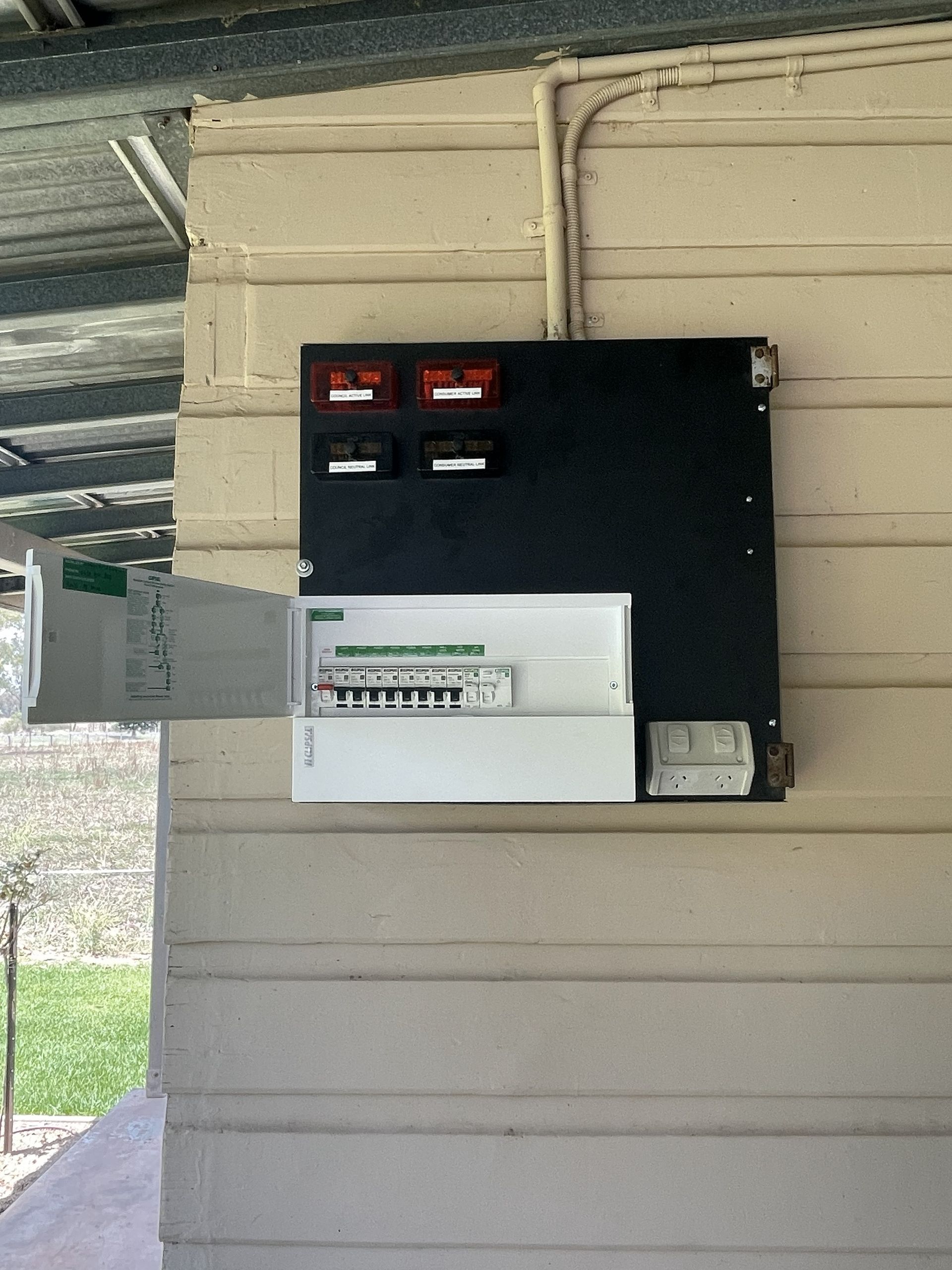 Electrical panel box on an exterior wall with open breaker panel. Black box with red/white digital displays.