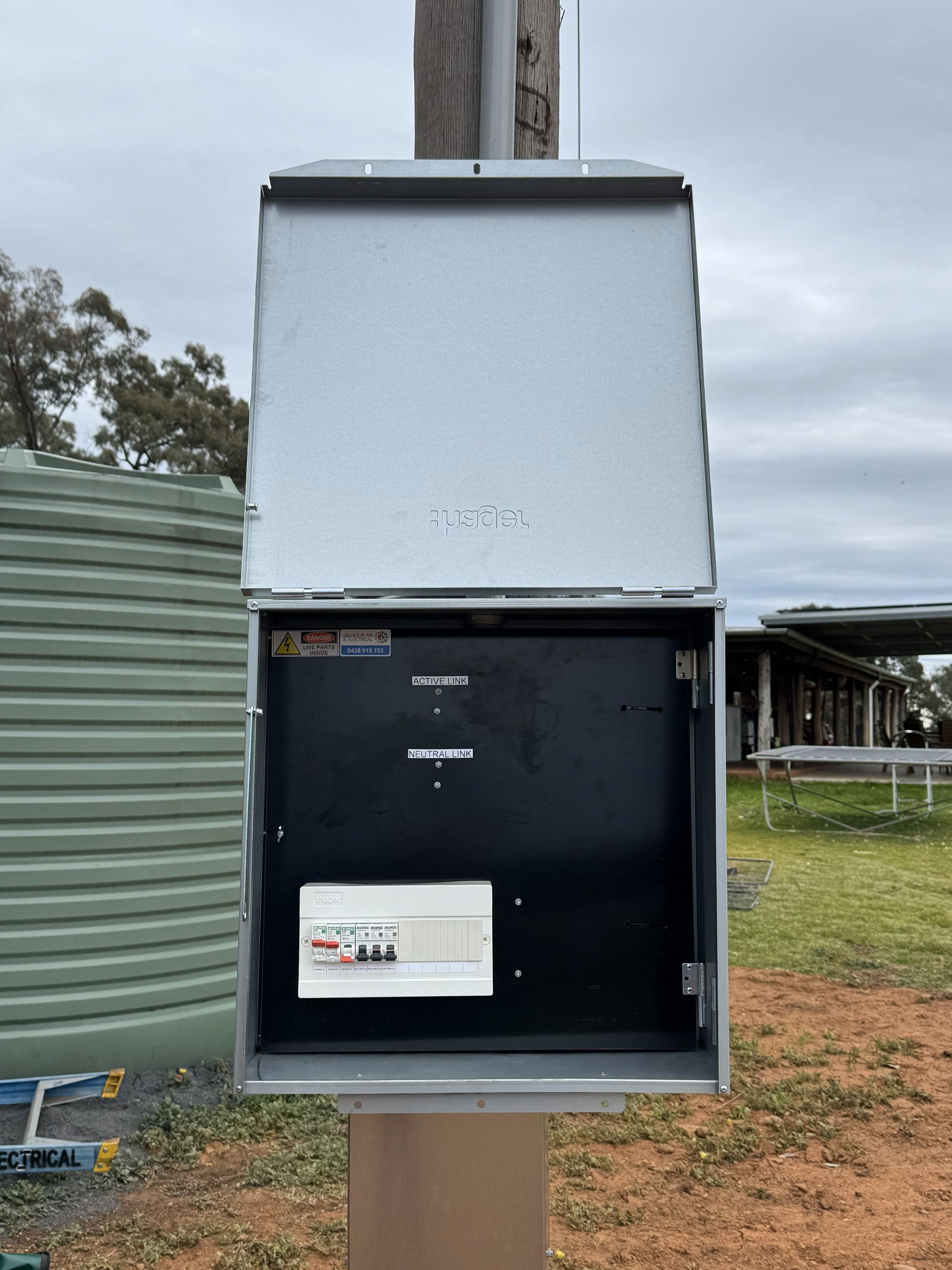 Opened gray electrical box mounted on a pole, showing wiring and circuit breakers, outdoors.