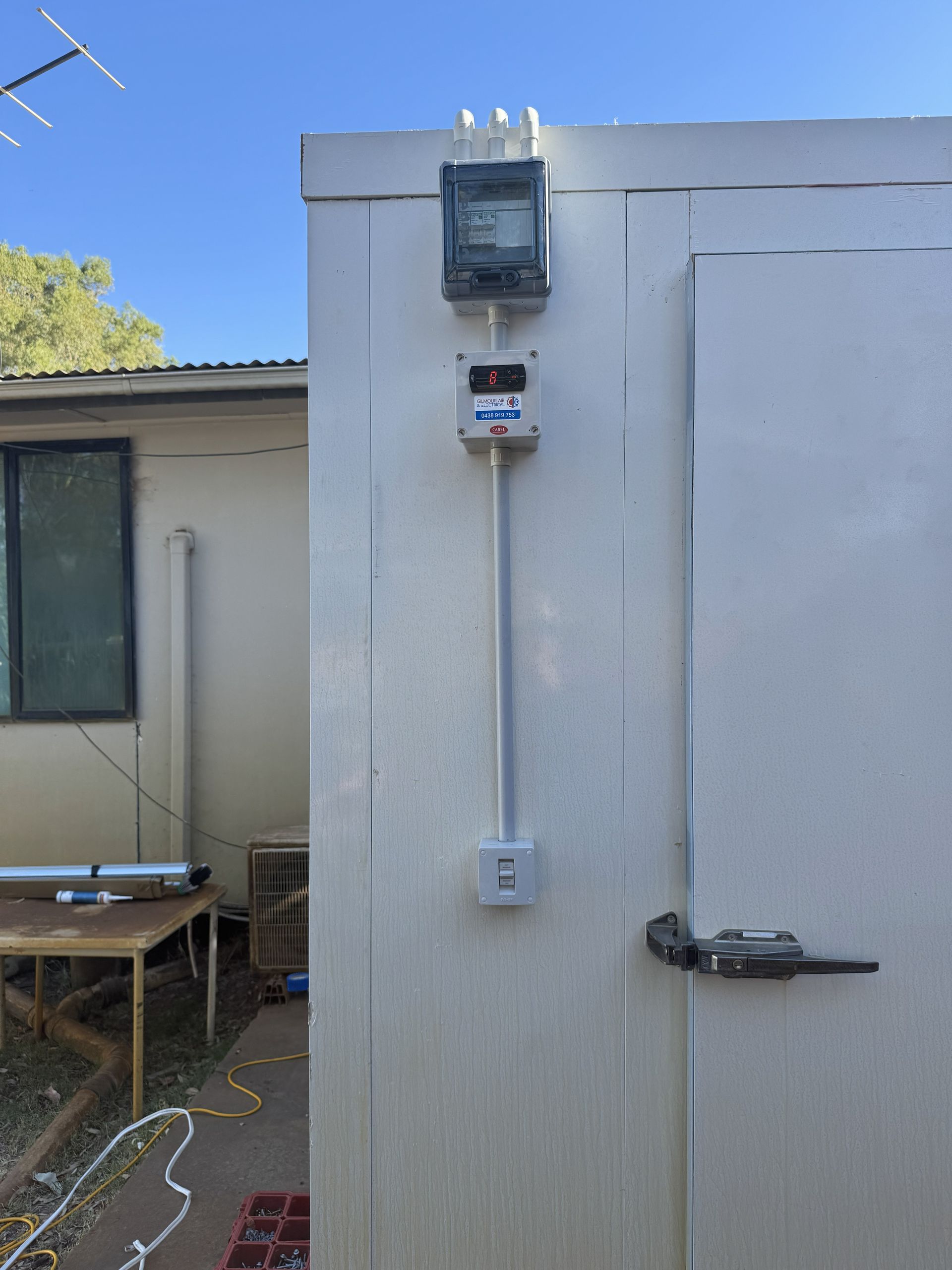 Electrical components mounted on a white, insulated building with a door.