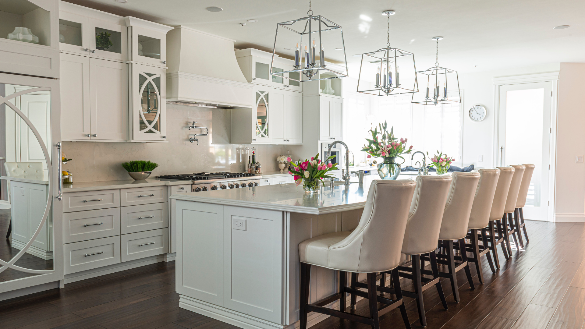 A kitchen with white cabinets , a large island , and a long row of chairs.