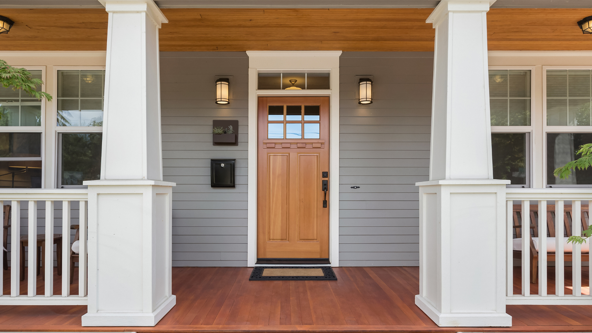 The front porch of a house with a wooden door and white pillars.