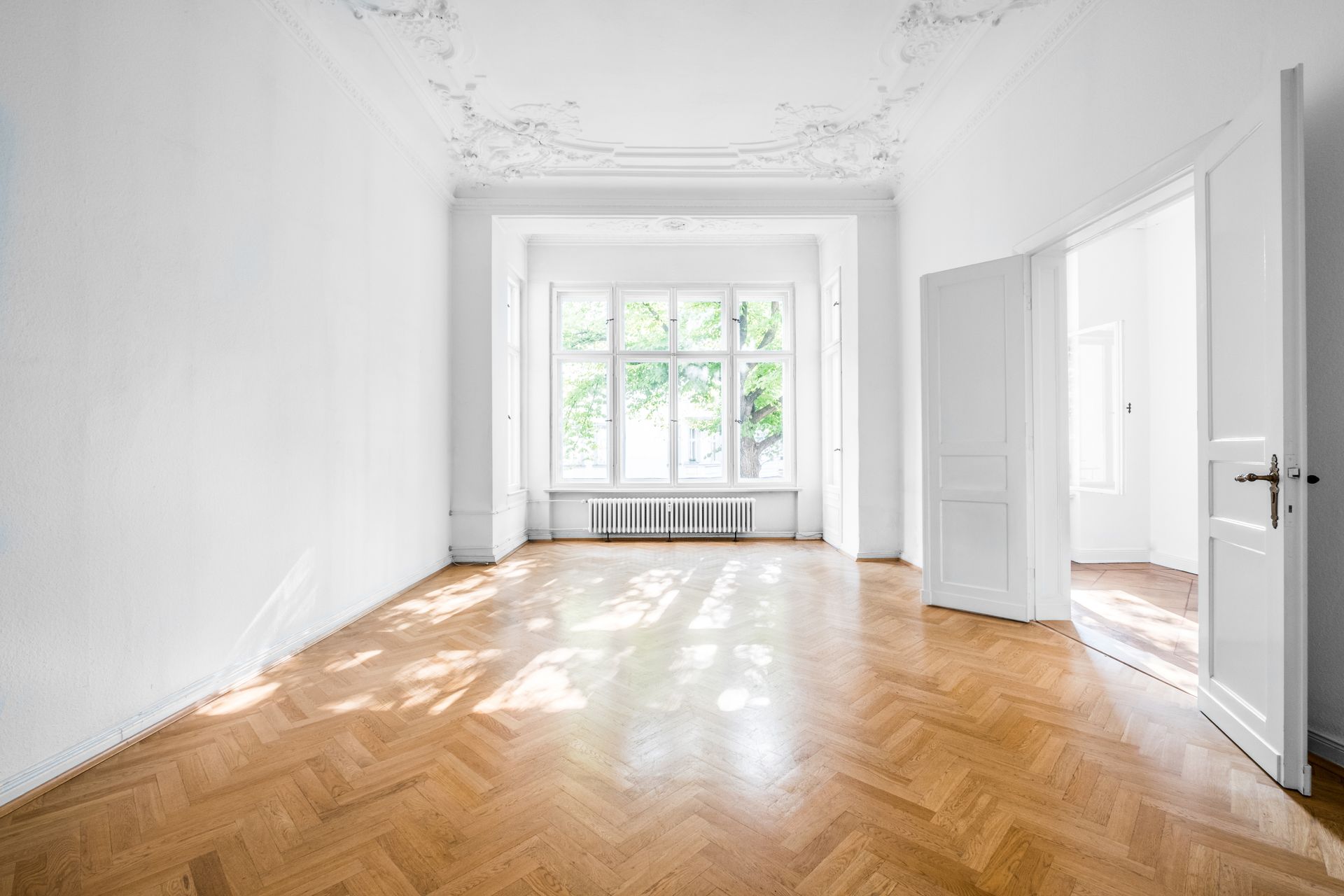 An empty living room with a wooden floor and white walls.