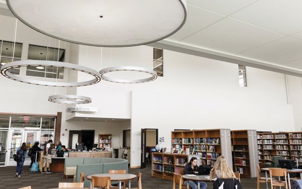 Modern library interior with students, bookshelves, and circular lights.