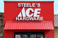 Steele's Ace Hardware storefront with red facade, white text and logo. Red awning over door.