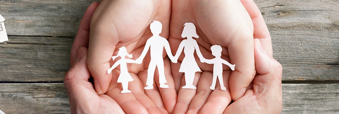 Hands holding a paper cutout of a family against a wooden background.