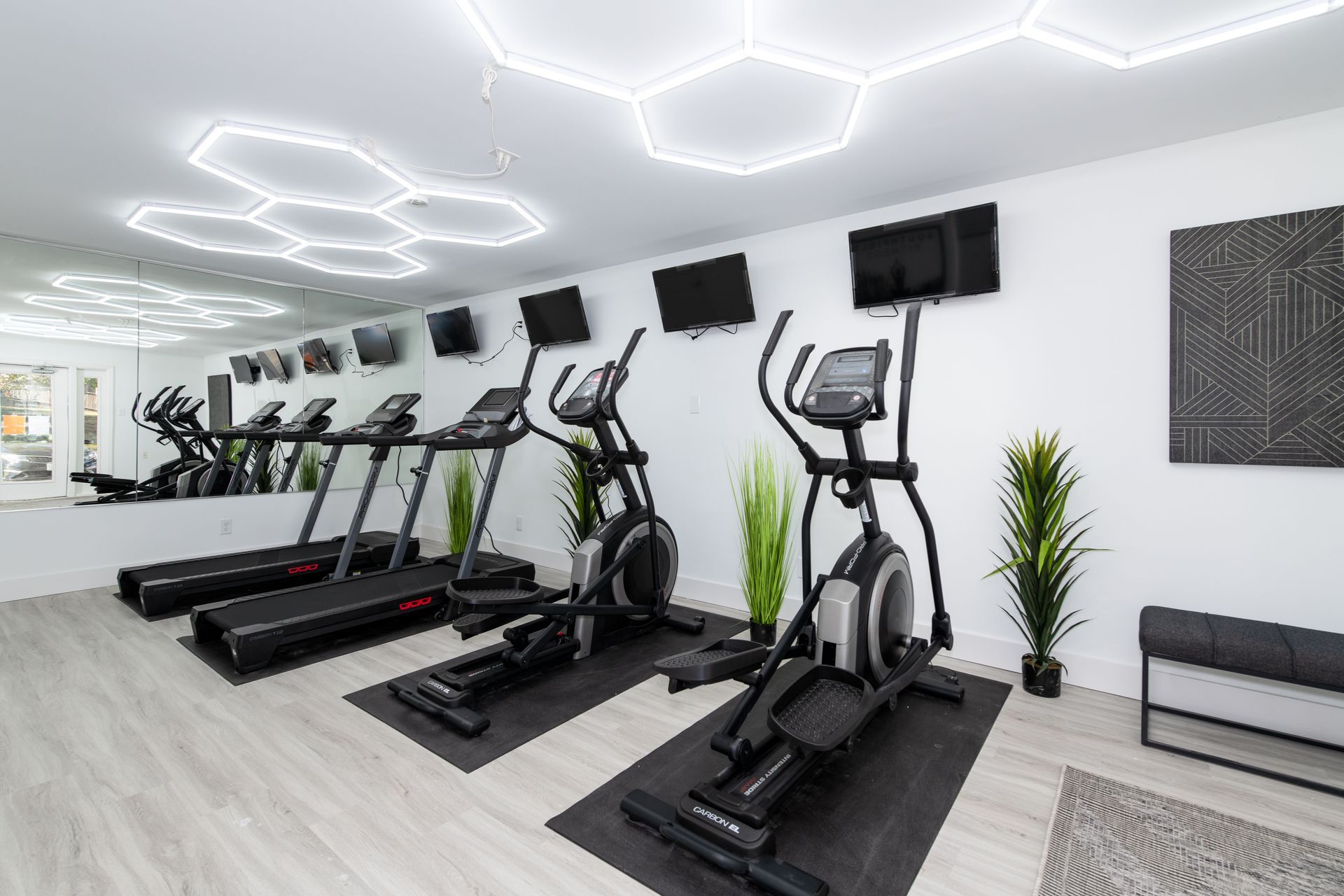 A gym with treadmills , ellipticals , and a large mirror.