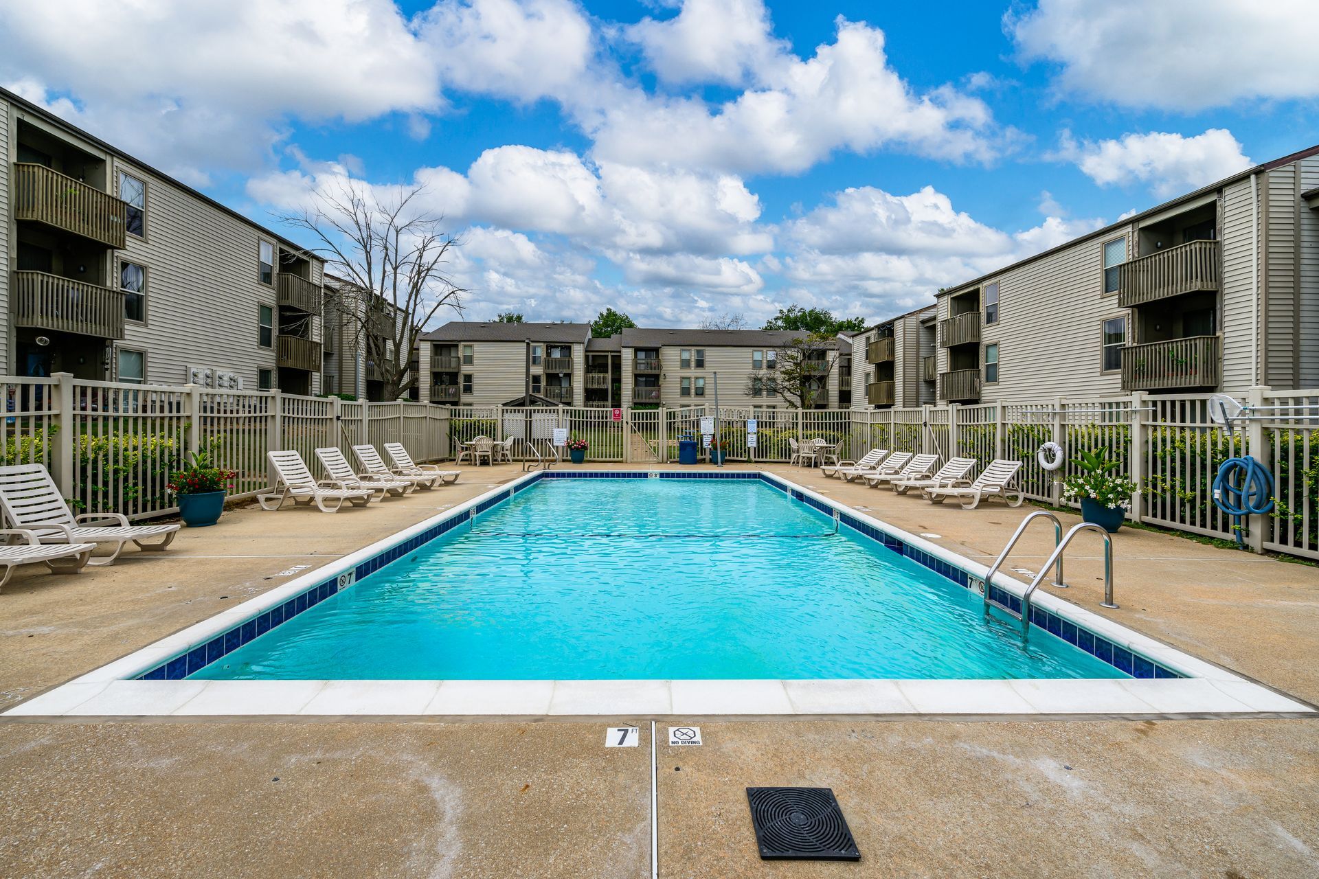 A large swimming pool surrounded by chairs and a fence in front of a building.