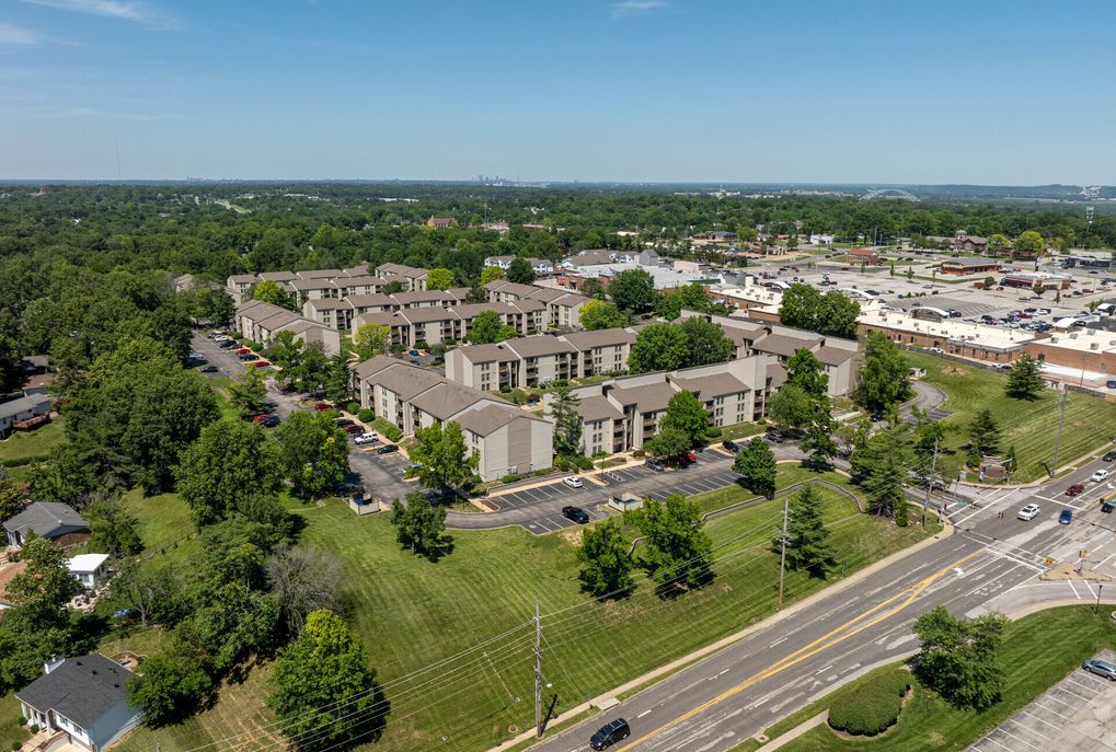 An aerial view of a large apartment complex surrounded by trees and a highway.