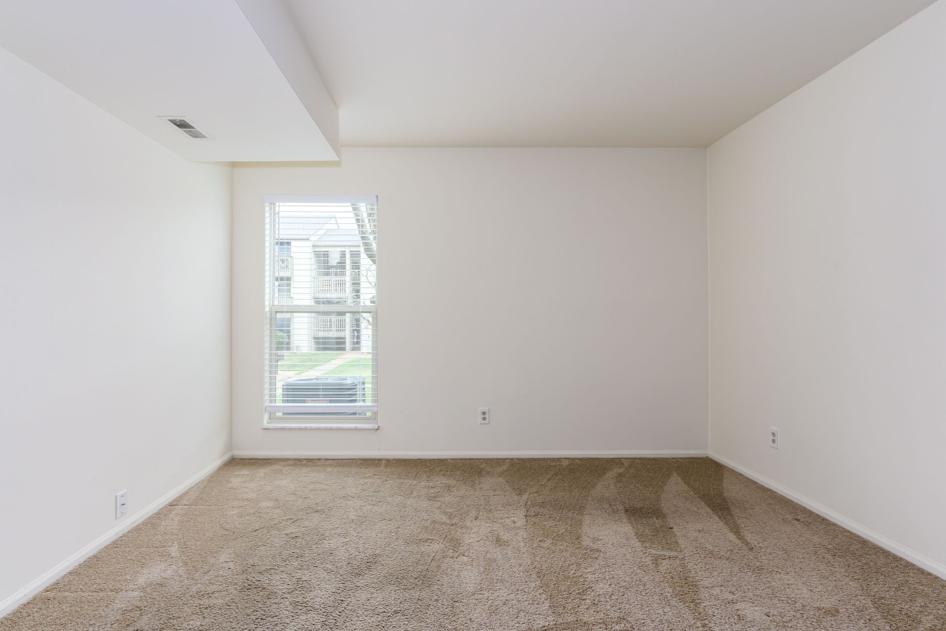 An empty room with a window and a carpeted floor.