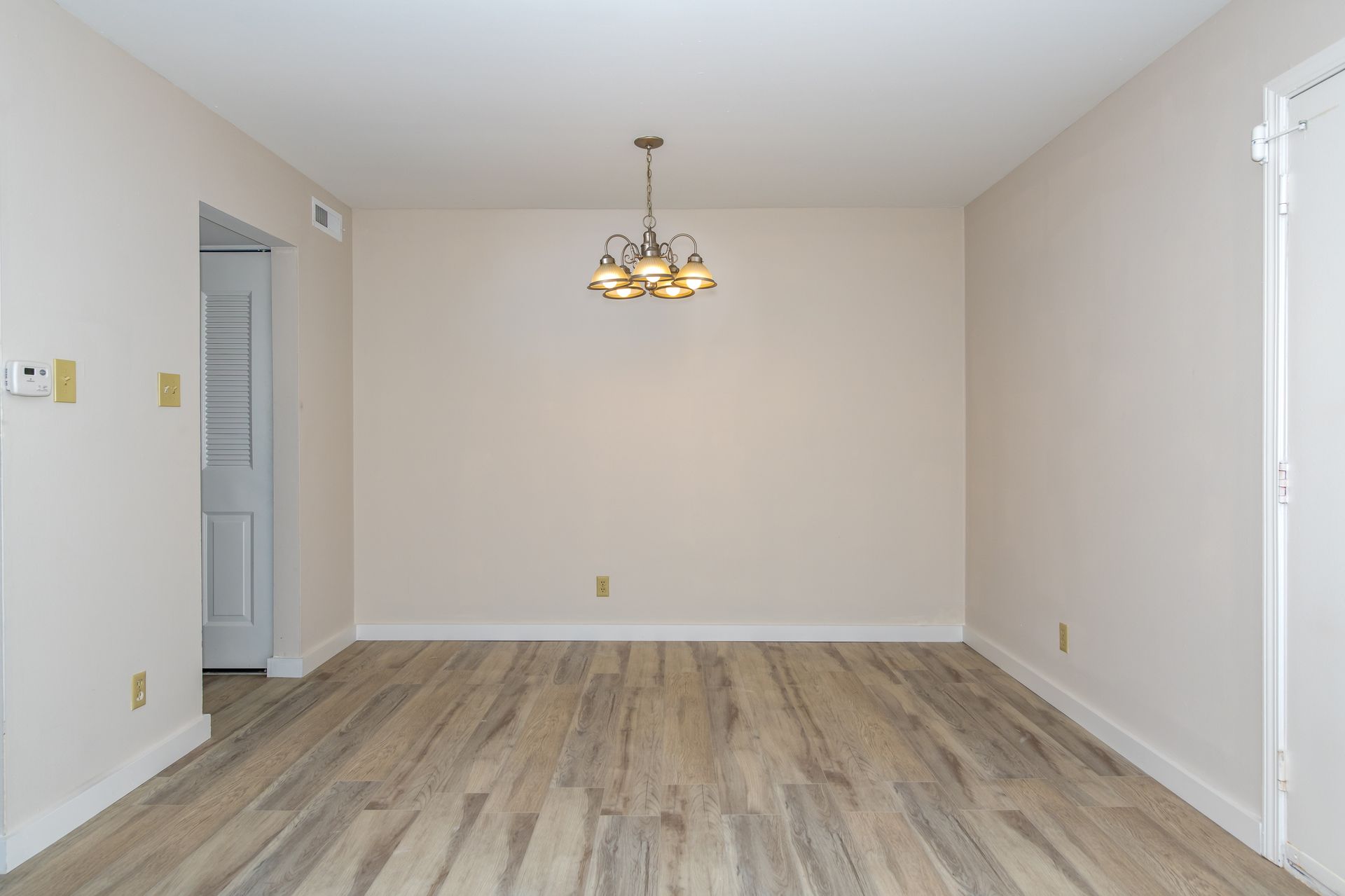 An empty dining room with hardwood floors and a chandelier.