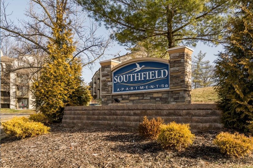 A sign for southfield apartment complex is surrounded by trees and bushes.