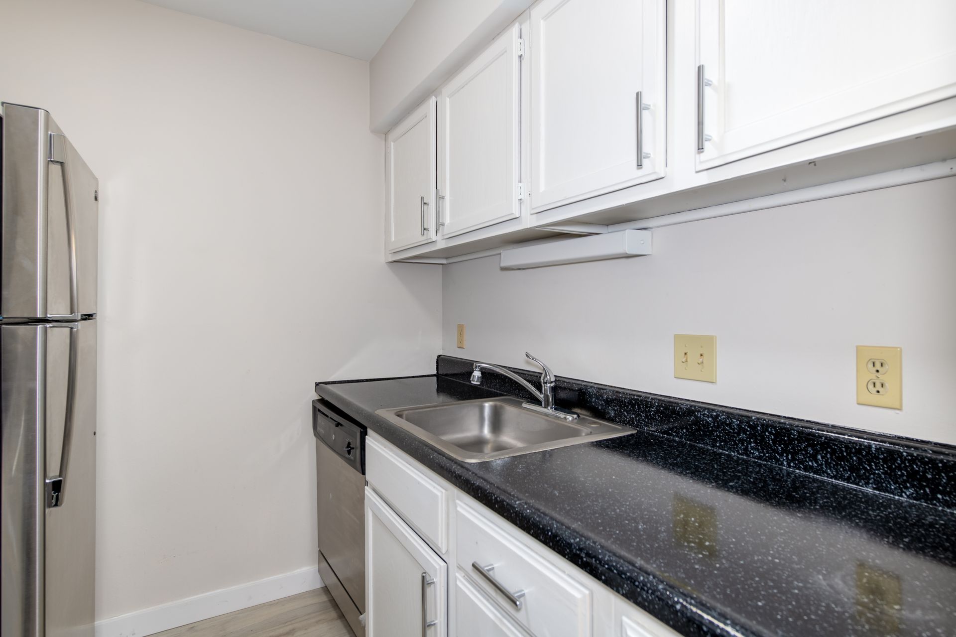 A kitchen with white cabinets , a sink , a refrigerator , and a dishwasher.