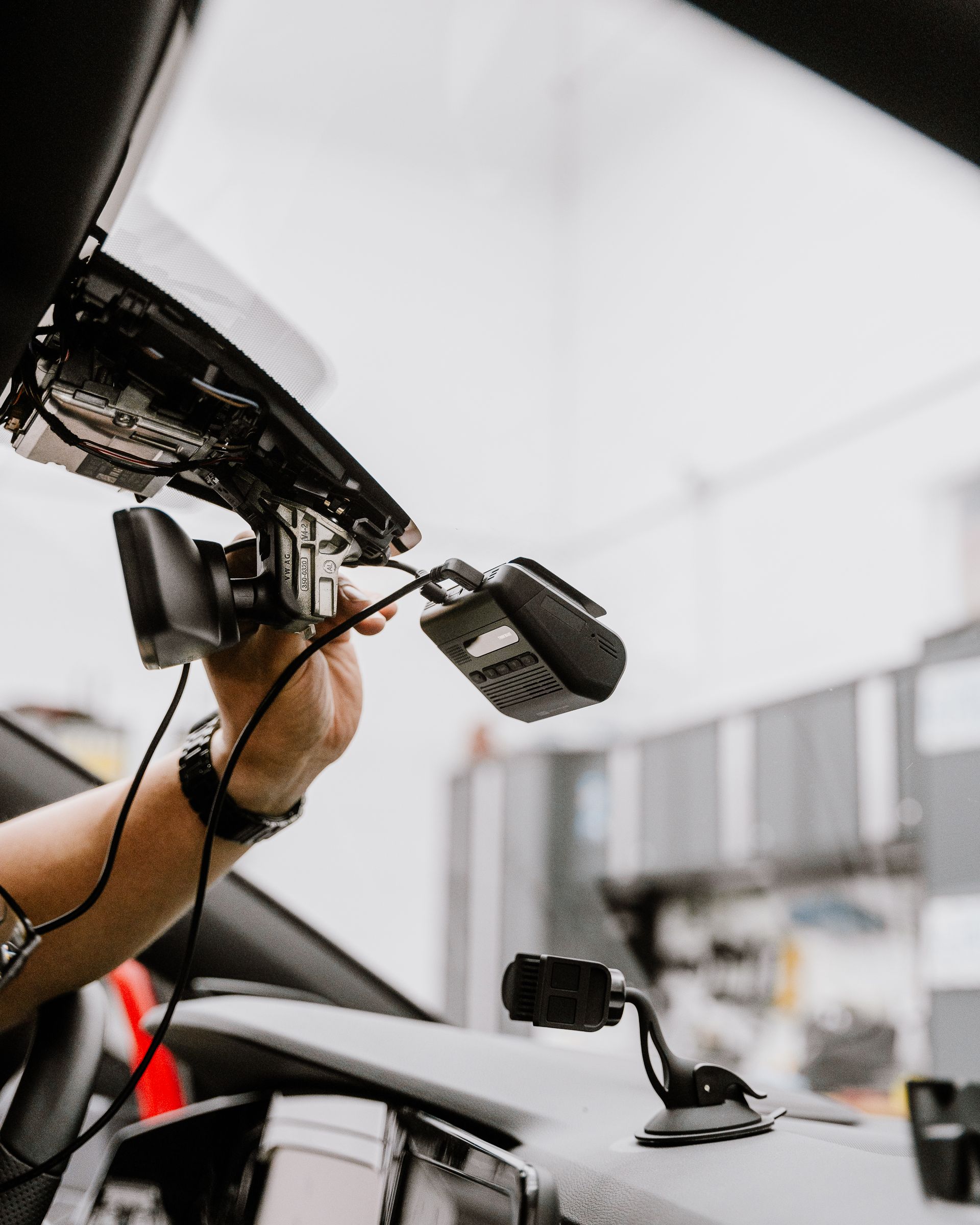 A person is holding a camera attached to the rear view mirror of a car.