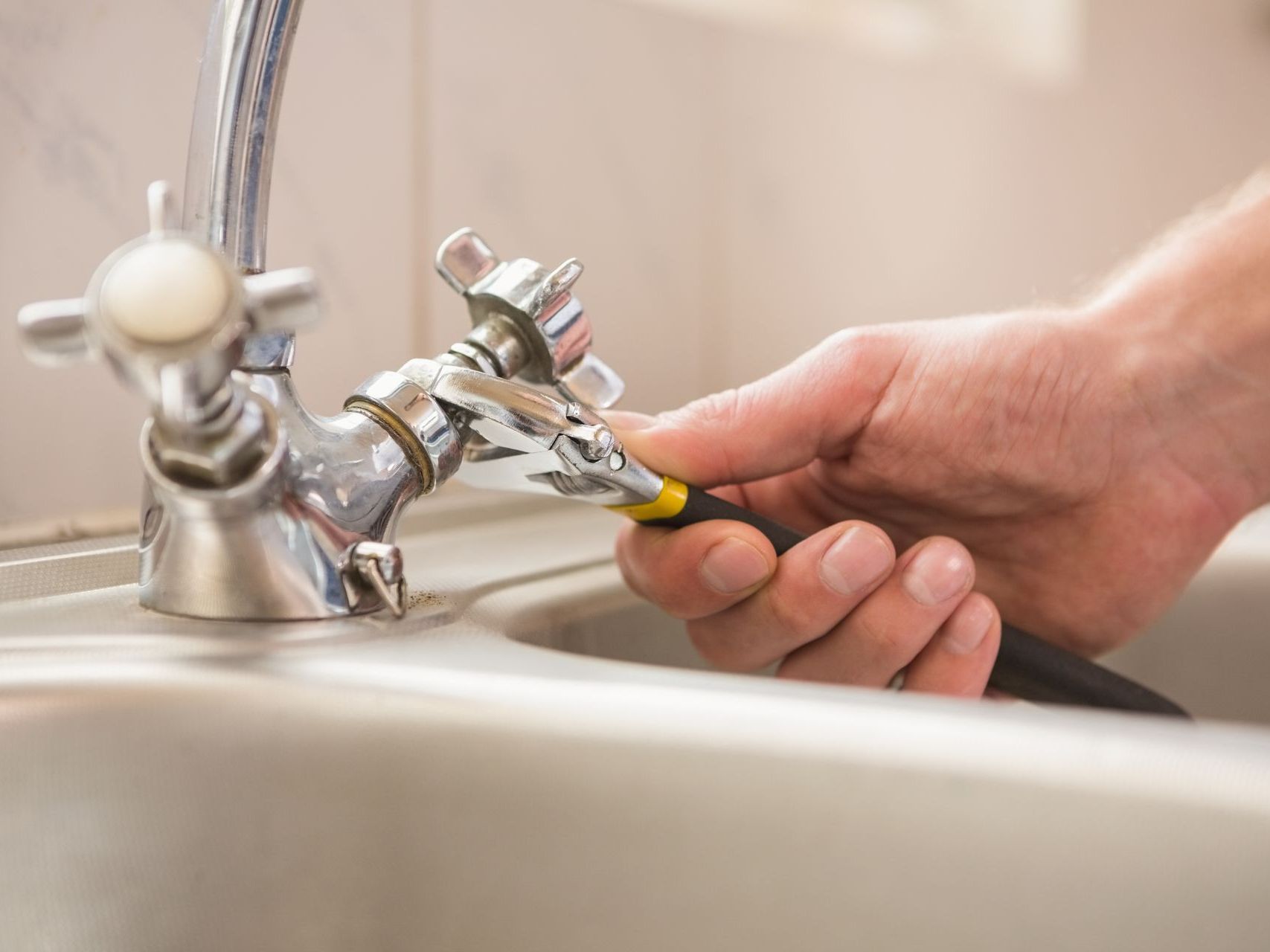 A person is fixing a sink faucet with a wrench.