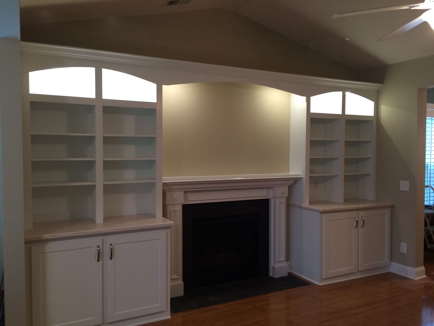 Built-in white bookshelves with cabinets frame a fireplace. Beige walls, wood floor.