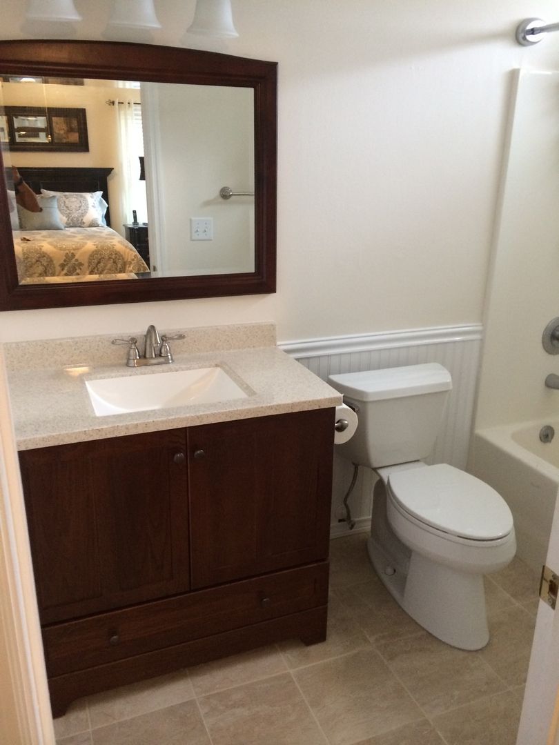 Bathroom with dark wood vanity, toilet, mirror, and a glimpse of a bed in the reflection.