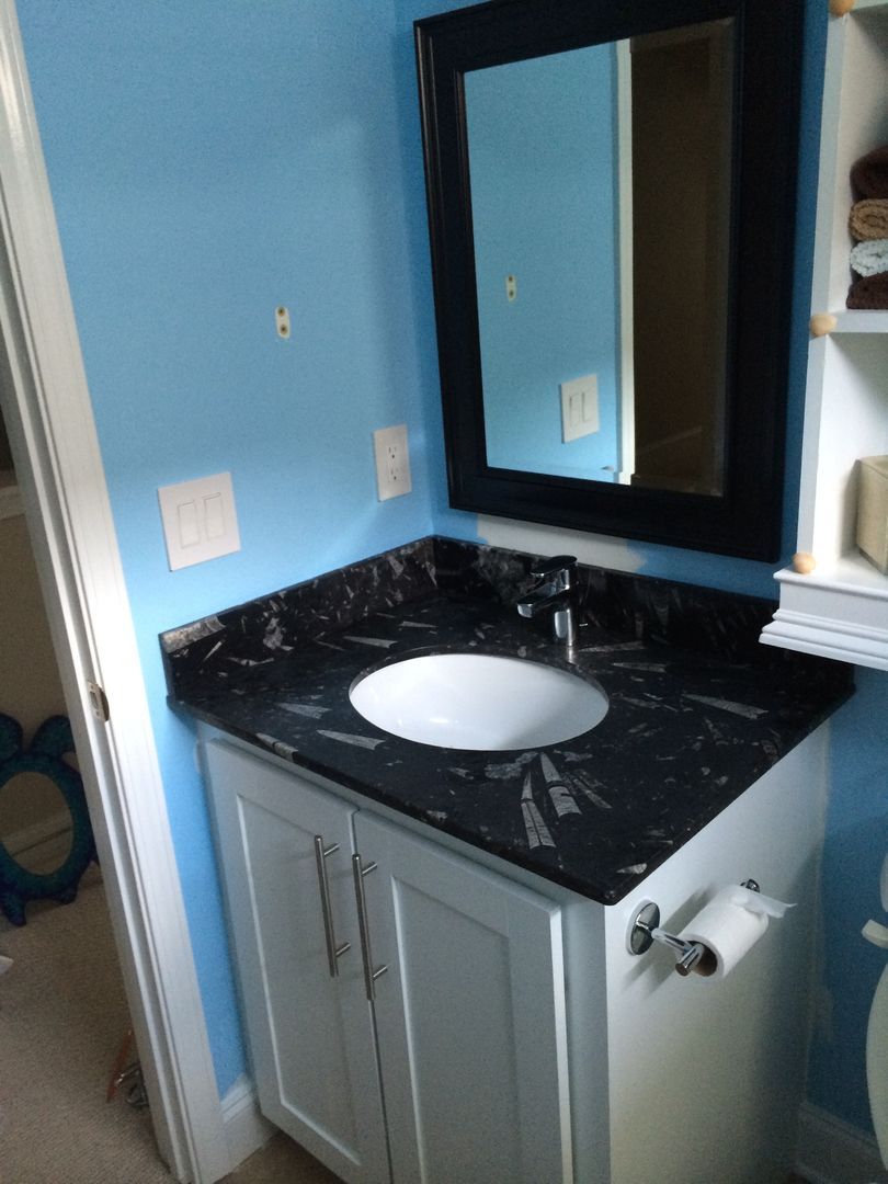 Bathroom vanity with a black countertop, white cabinet, and mirror on a light blue wall.