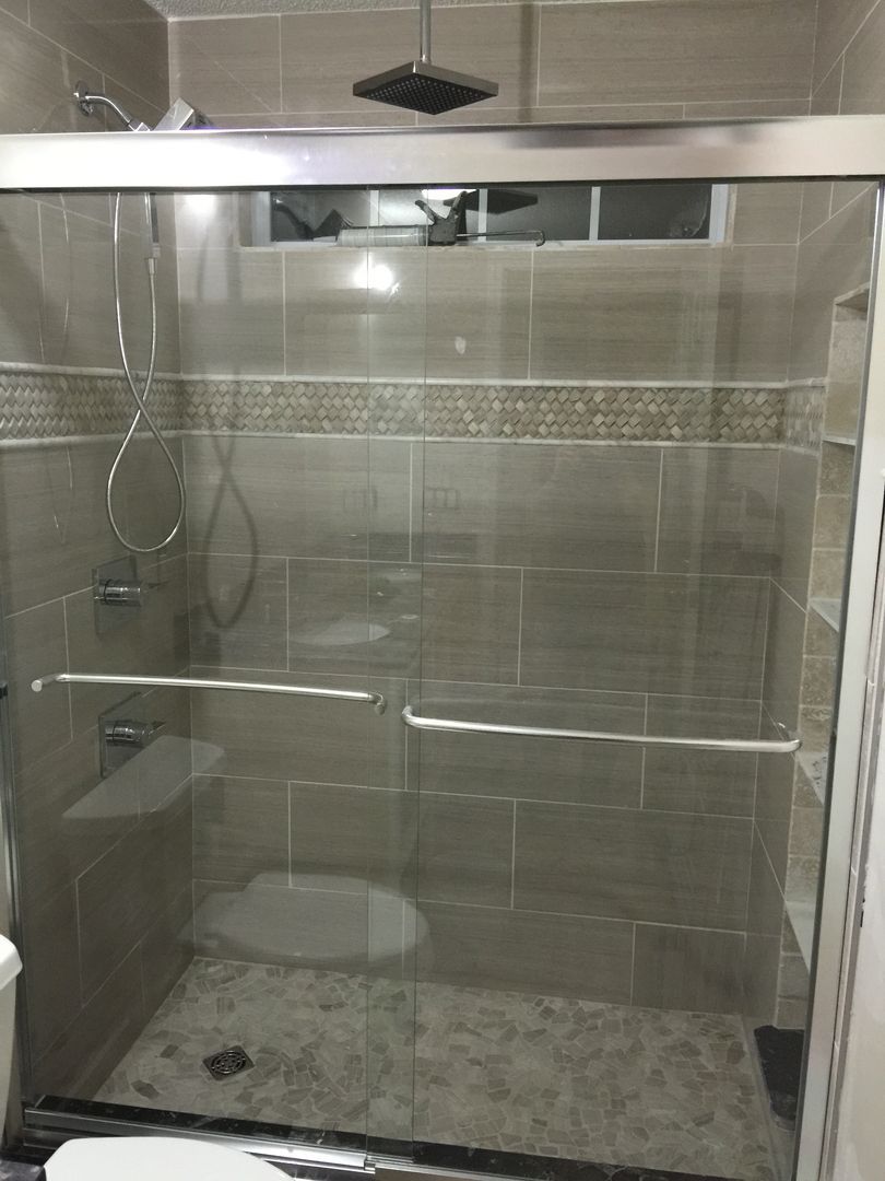 Shower stall with glass doors, tiled walls in beige with a mosaic border, square rain shower head.