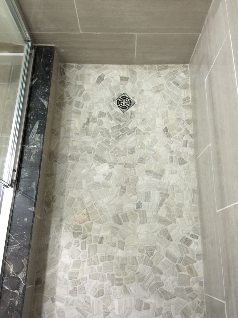 Shower stall with gray pebble tile floor and tile walls, drain in center.