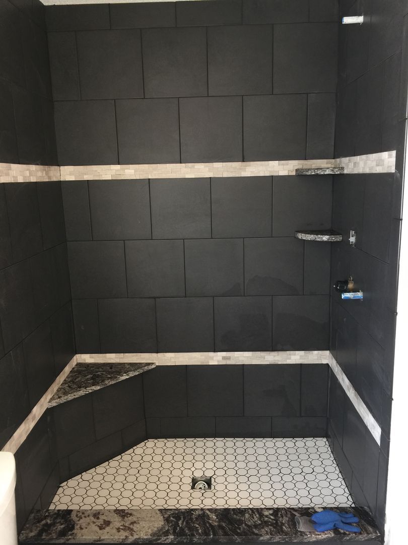 Black tiled shower with white and gray mosaic floor, silver fixtures, and gray bands.
