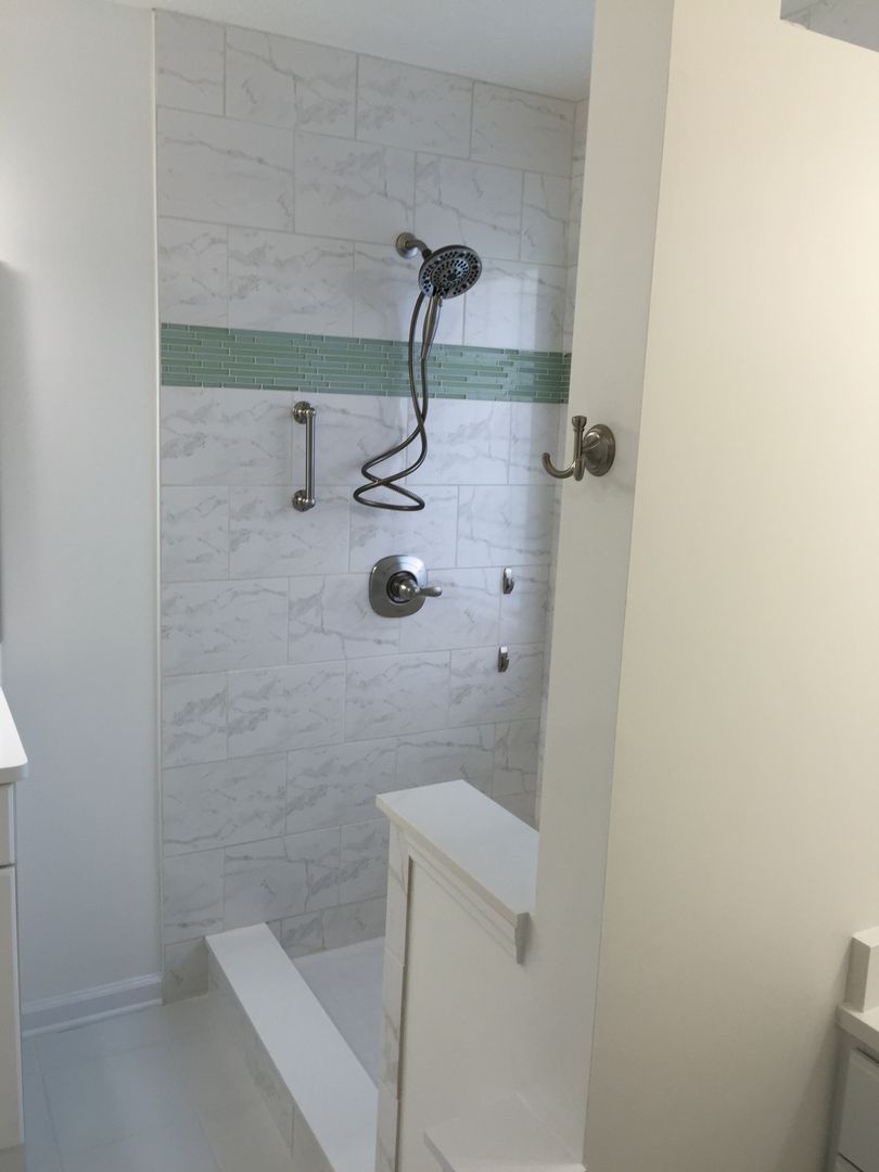 Accessible shower with grab bar, built-in seat, and hand-held showerhead. White tile with a green accent stripe.
