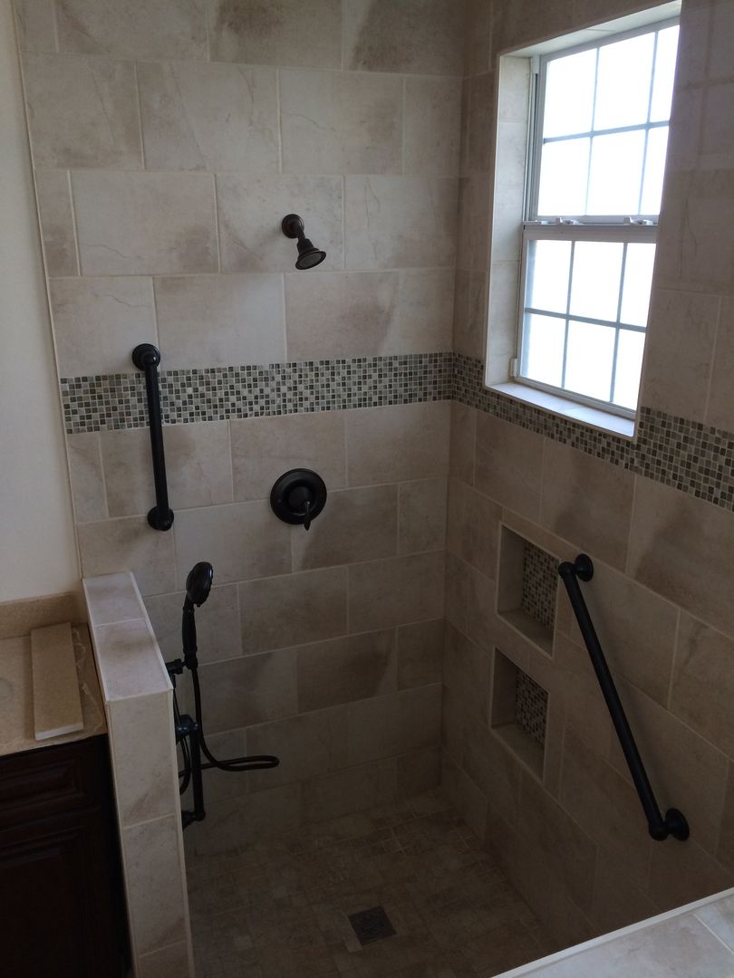 Accessible shower with beige tile, dark fixtures, and grab bars. Features a window and built-in shelves.