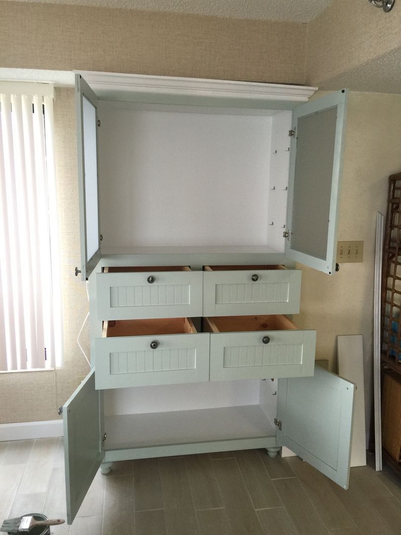 Light blue cabinet with open doors and drawers in a room.