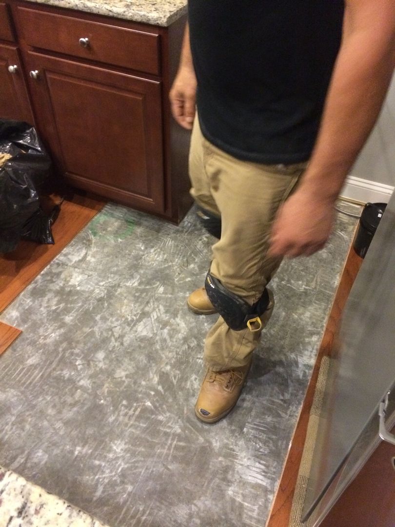 Person wearing ankle weights, standing on a patterned floor in a kitchen next to wooden cabinets.