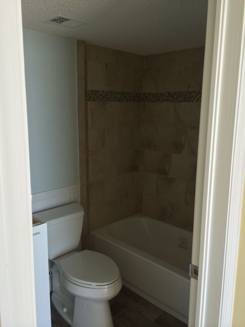 Bathroom with toilet and tub, light blue wall, tan tile surround, and white trim.