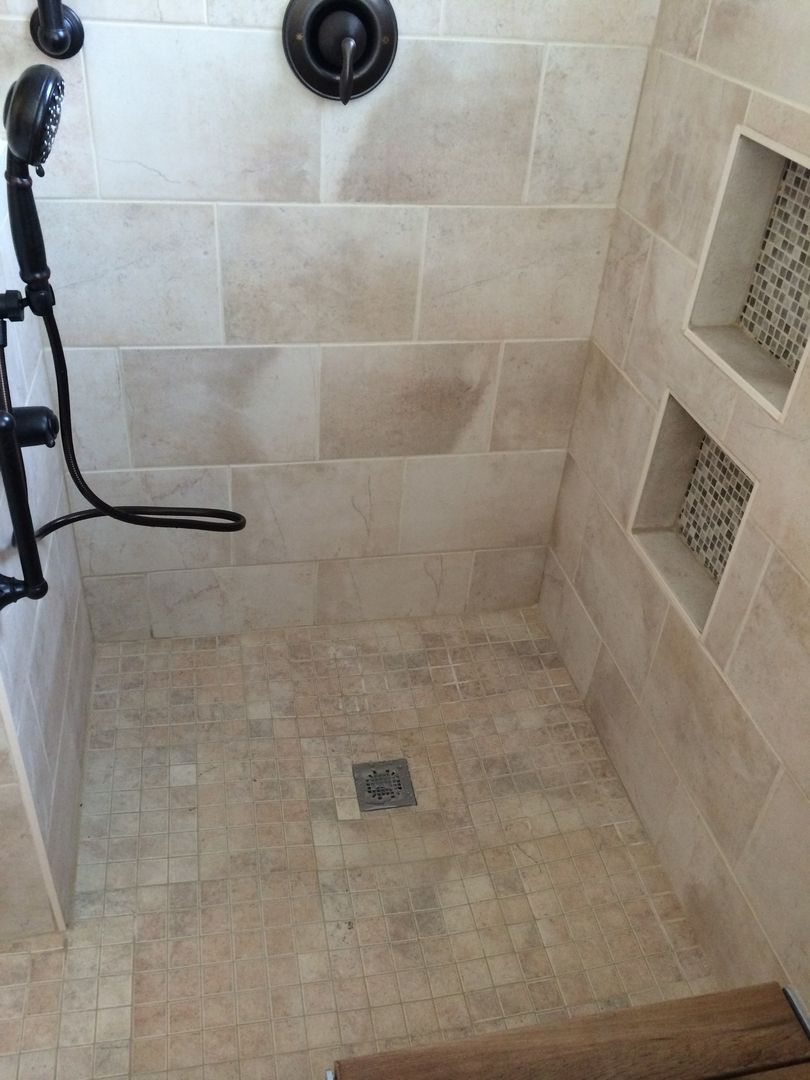 Beige tiled shower with dark fixtures and two built-in niches with patterned tile.