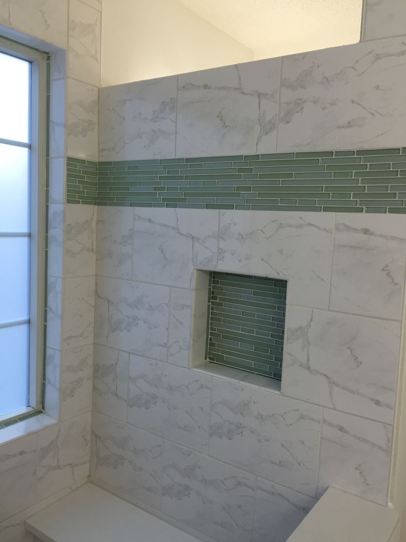 Bathroom shower with white marble-look tiles, green accent band and niche with green mosaic. Window on left.