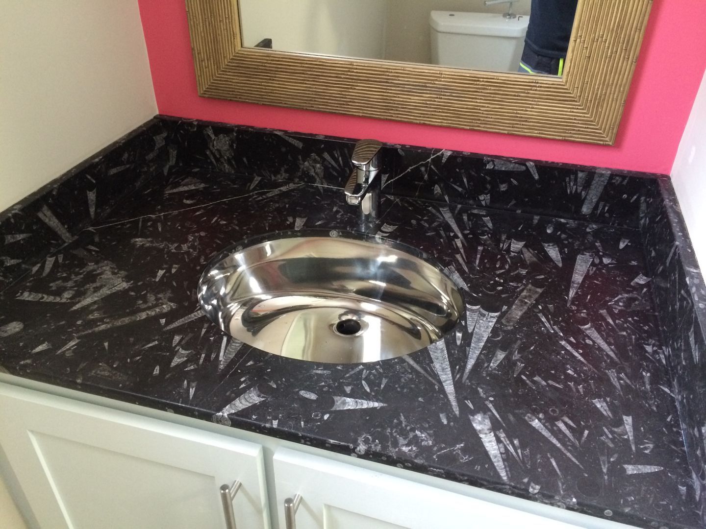 Black countertop with a stainless steel sink, set against a pink wall and light blue cabinet.