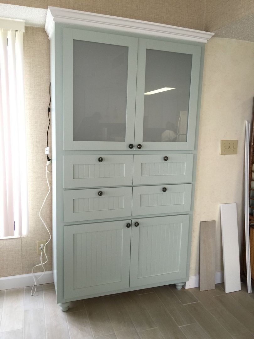 Tall blue-green cabinet with glass doors, drawers, and lower doors; in a room.