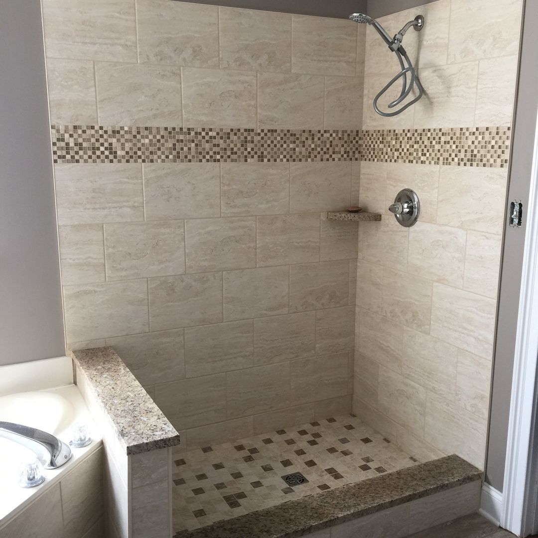 Shower stall with beige tiles, mosaic band, and stone floor.