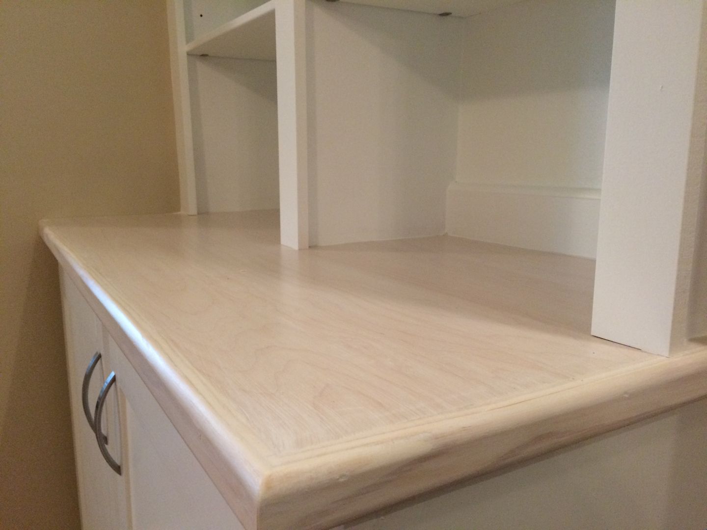 White cabinet with light-colored wooden countertop; built-in shelves above.