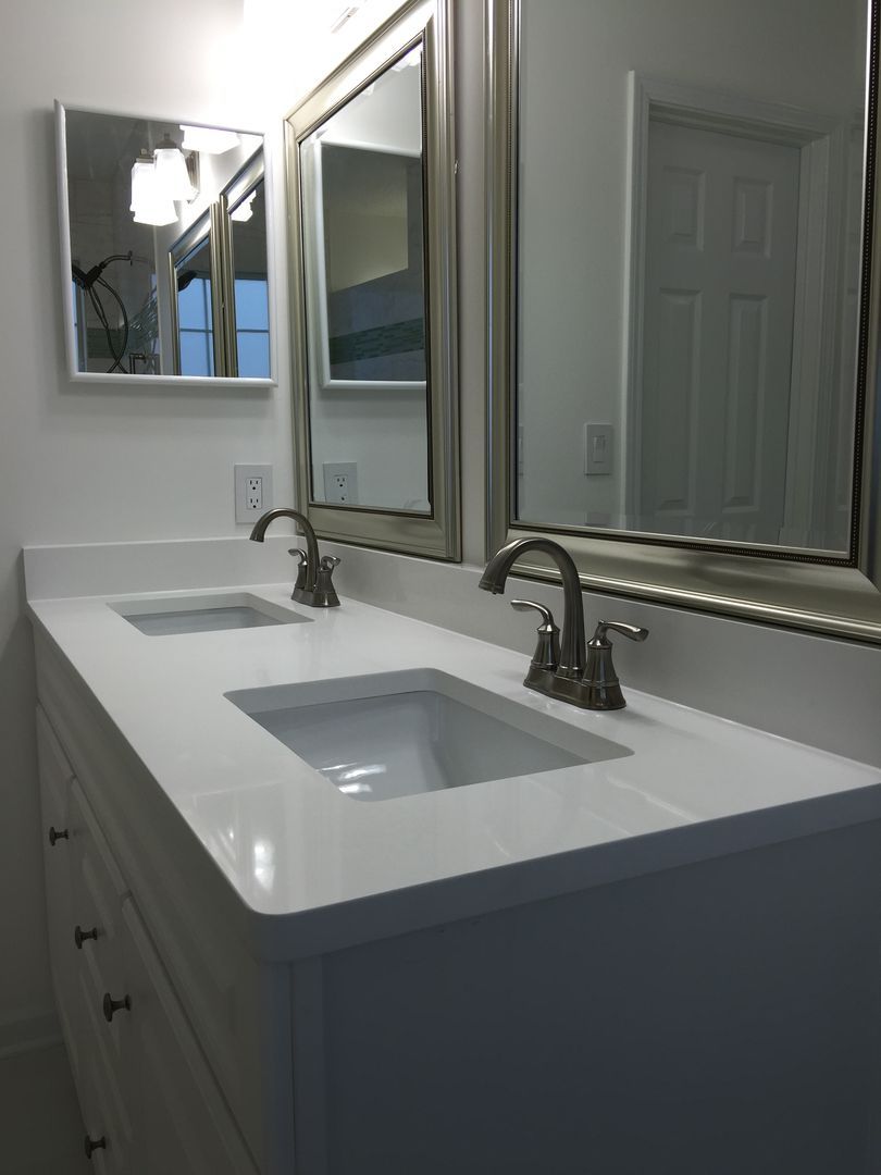 Bathroom vanity with two sinks, white countertop, silver fixtures, and mirrors. White cabinet with drawers.