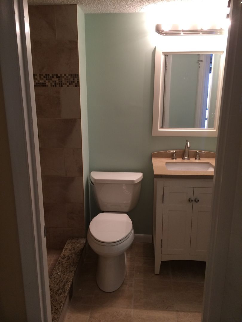 Bathroom with a white toilet, sink, and vanity. Soft green wall, stone tile shower.