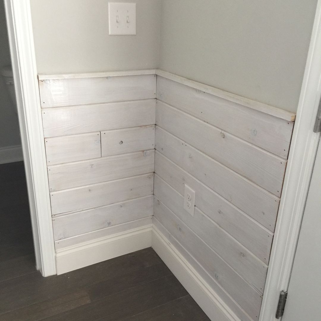 White shiplap wainscoting on a corner wall, with a white outlet, trim, and light gray upper wall.