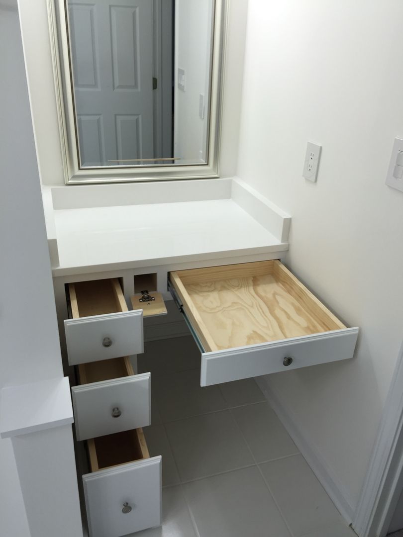 White vanity with drawers and pull-out desk in a small alcove, mirror above.