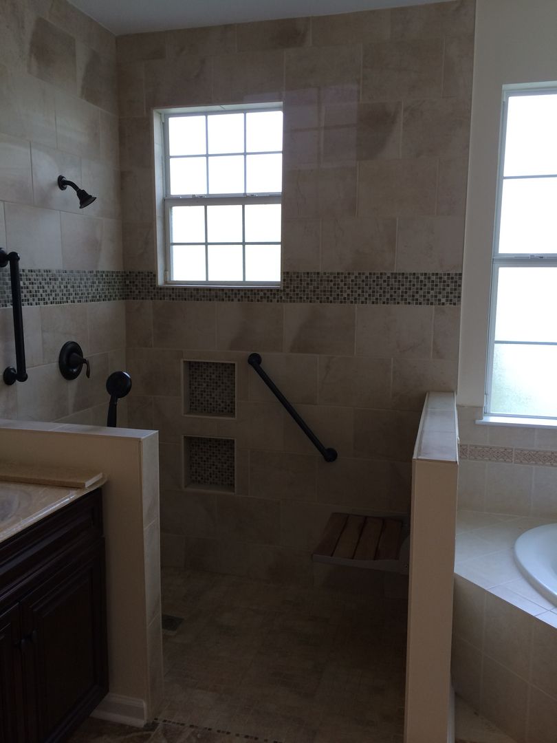Accessible walk-in shower with stone tile, grab bar, built-in seat, and two windows.