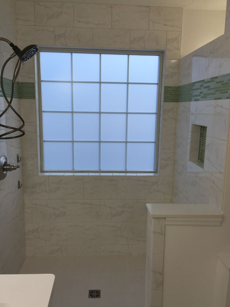Bathroom with a frosted window, white tile walls, a showerhead, and a built-in shelf.